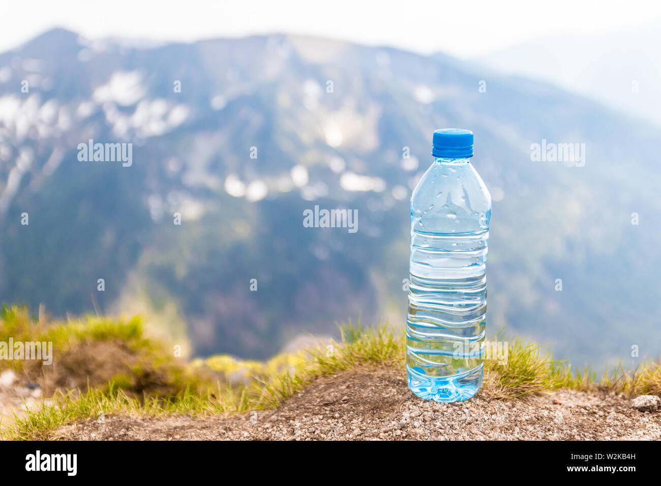 Plastic bottle with fresh drinking water stands on a stone high in the mountains on a sunny day. Stock Photo