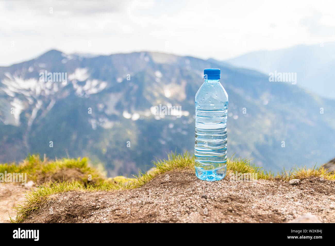 Clear water in a plastic bottle stands on a stone high in the mountains on a sunny day. Stock Photo