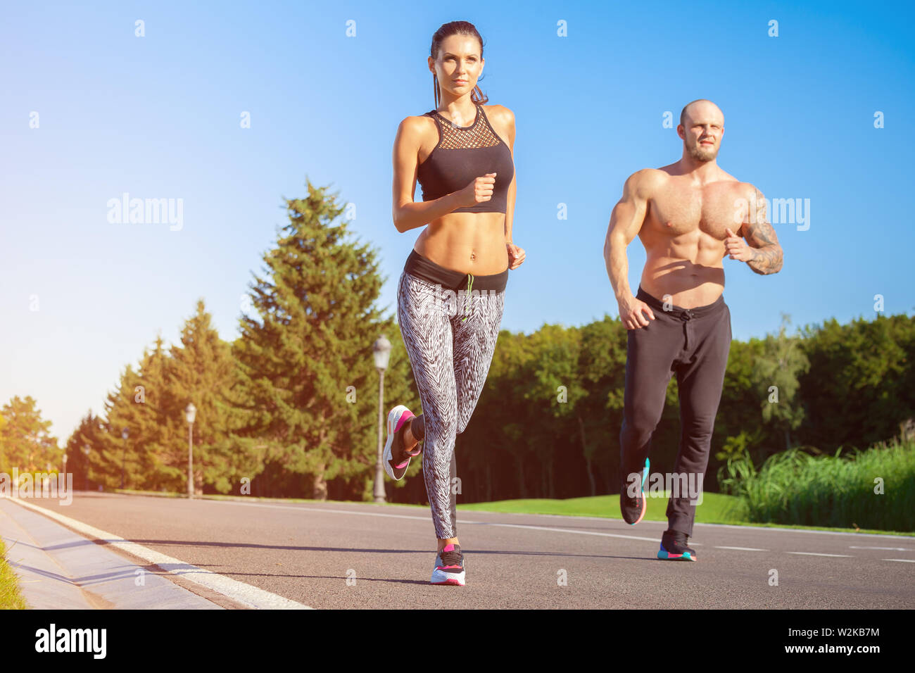Young strong male and female fitness models outdoors in beautiful landscape. Man and woman running in park at sunset Stock Photo