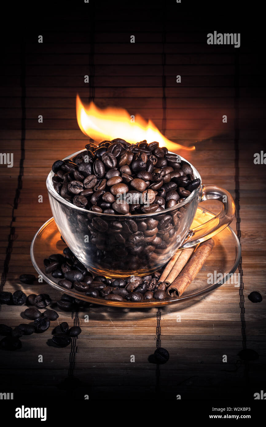 Steaming cup of coffee, cinnamon sticks and a coffee beans on fire