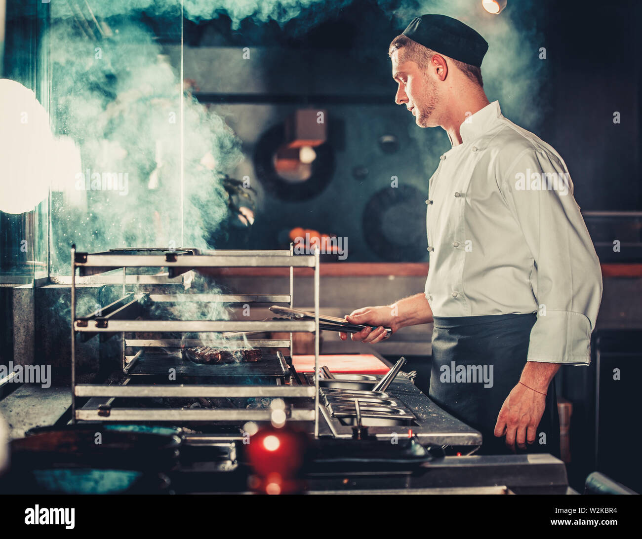 Young male cook preparing meal on the grill in kitchen Stock Photo