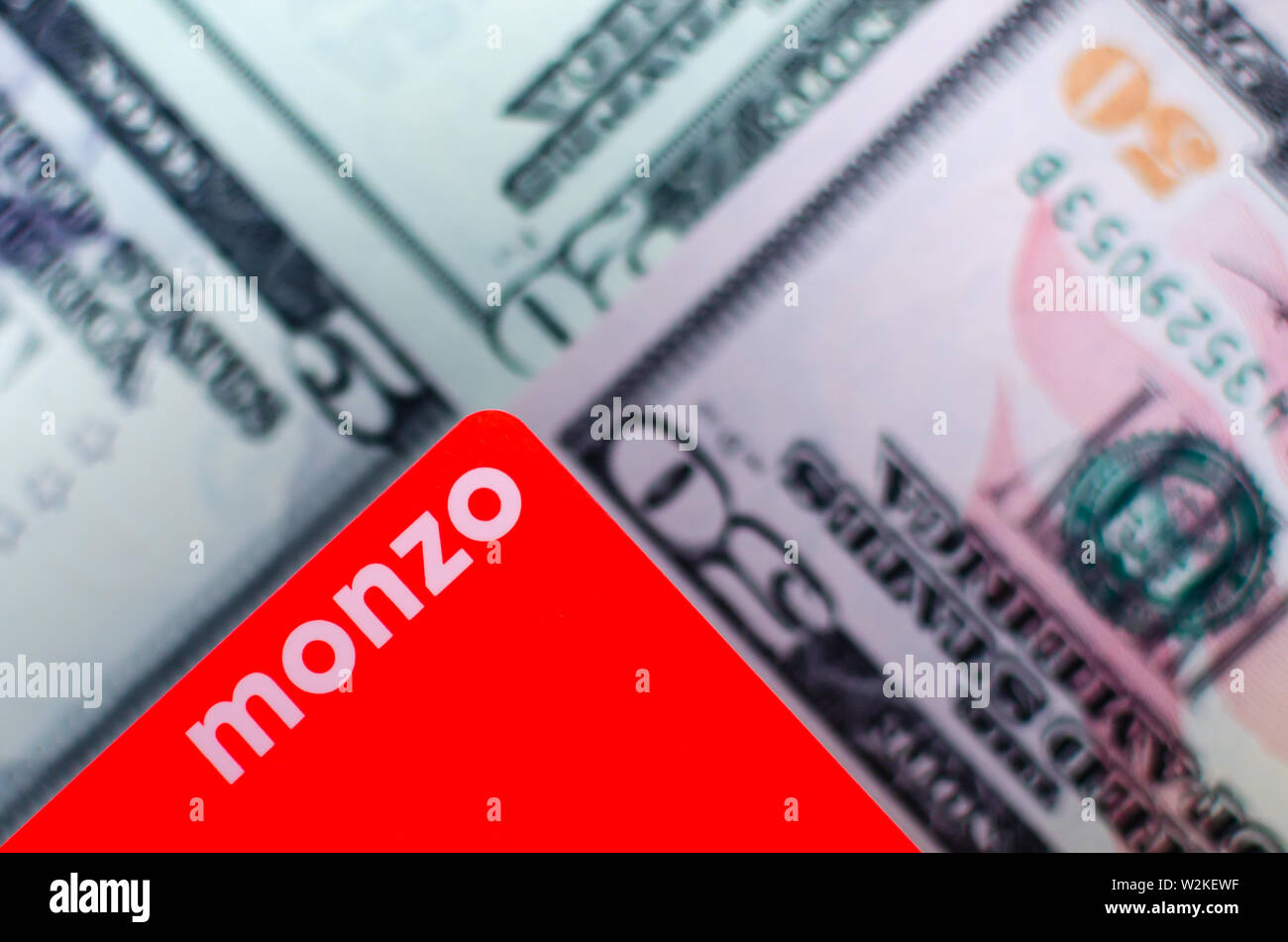 Monzo Bank cards on a blurred background of dollar bills different denominations. Stock Photo