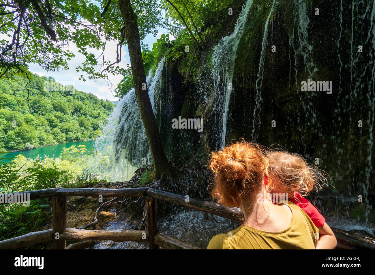 Mother carrying 3 years old girl in front of a rock face where pure fresh water rushing down the edge - Plitvice Lakes National Park in Croatia Stock Photo