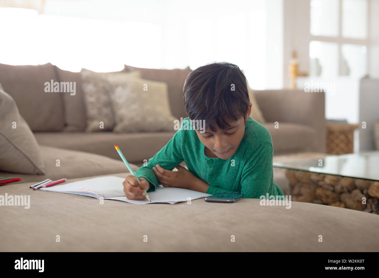 Boy using mobile phone while drawing a sketch on book at home Stock Photo