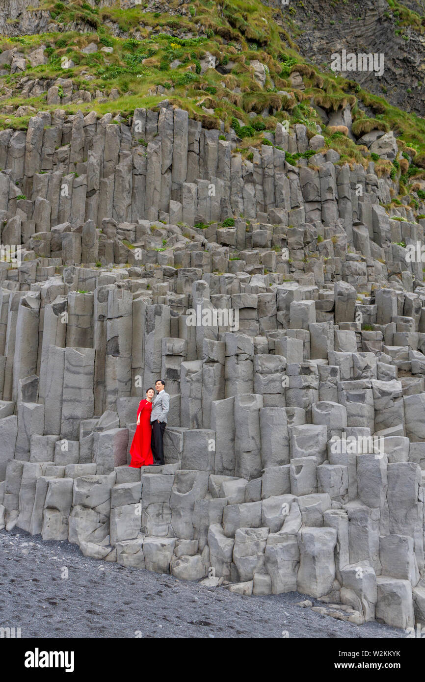 A wedding couple having photos taken on basalt columns on Reynisfjara black sand beach, southern Iceland. Stock Photo