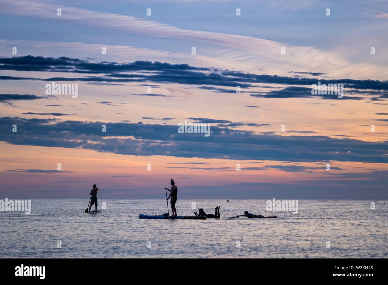 Aberystwyth Wales UK, Tuesday 09 July 2019  UK Weather: People silhouetted against the colours of the sunset as they paddleboard on the flat calm sea off the beach in Aberystwyth at the end of a warm summers day  in west Wales.   photo credit: Keith Morris//Alamy Live News Stock Photo