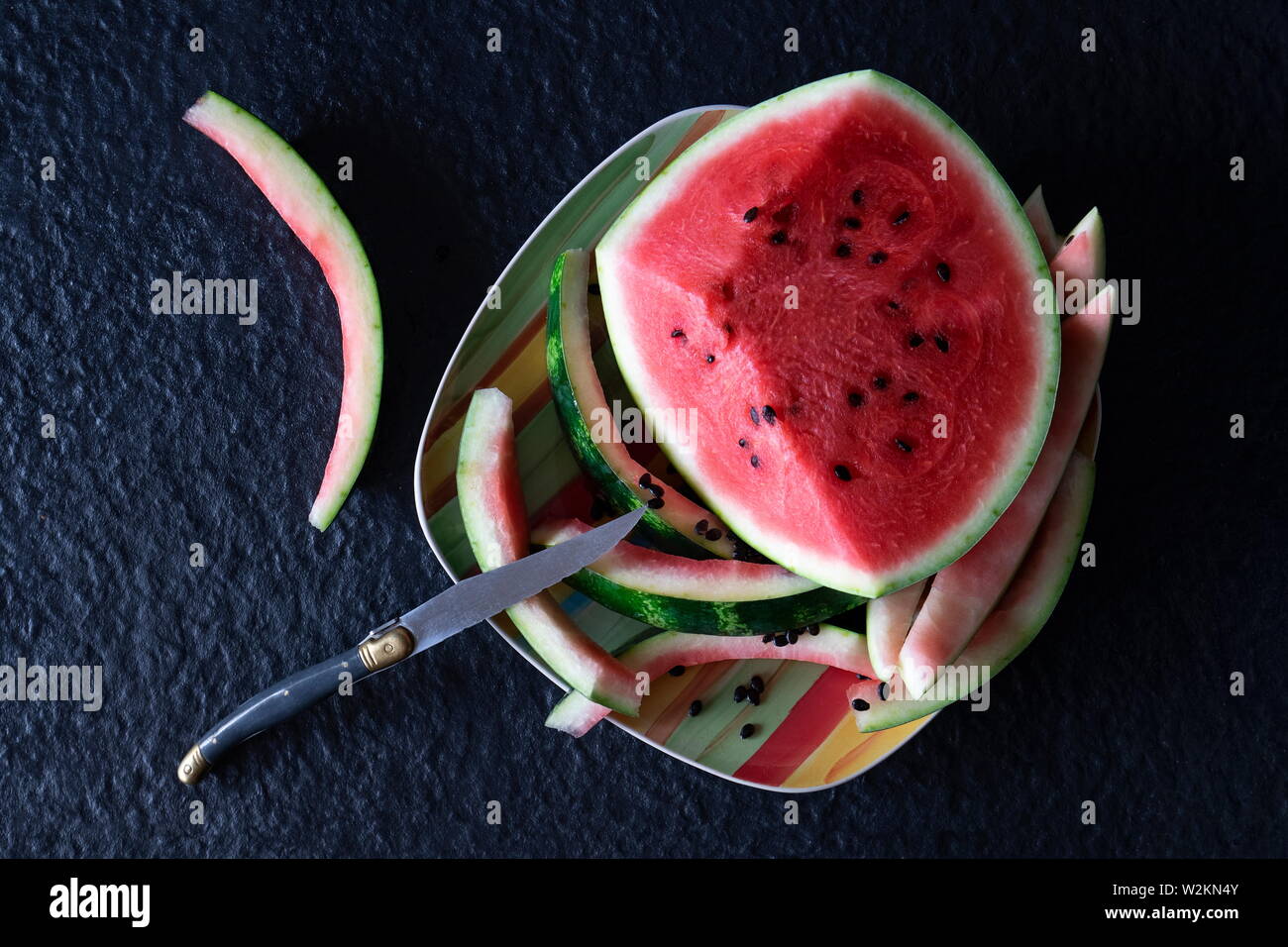 Piece of red watermelon with cut slices and eaten on a plate with a knife on a black background Stock Photo