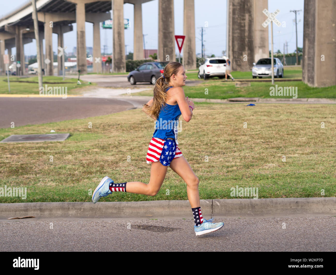 A young woman wearing red, white and blue attire running the final stretch of the Four For the Fourth / 4 Mile Fun Run in Corpus Christi, Texas USA. Stock Photo