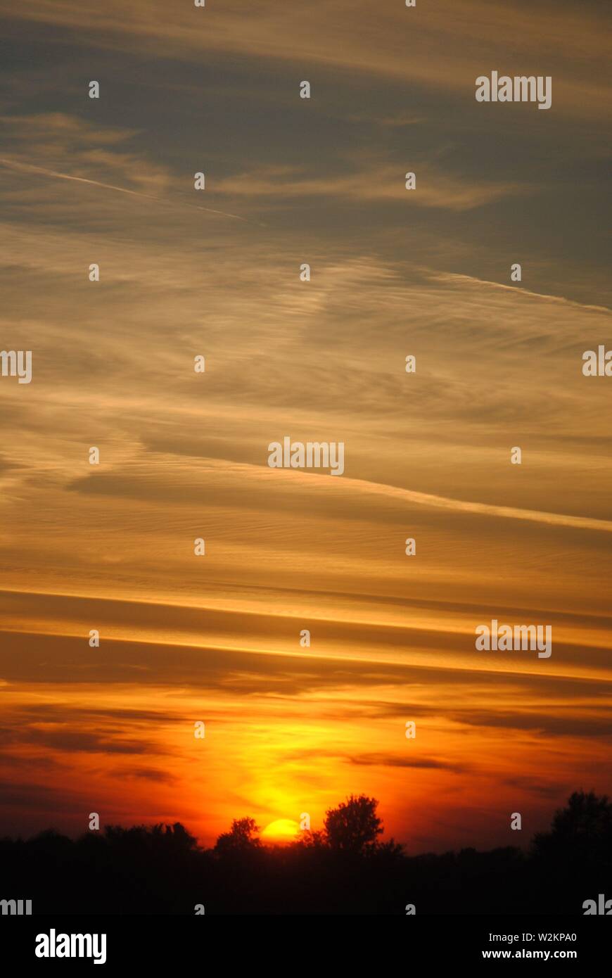 strong orange and yellow natural sunset with silhouette foreground and patterned clouds. Stock Photo