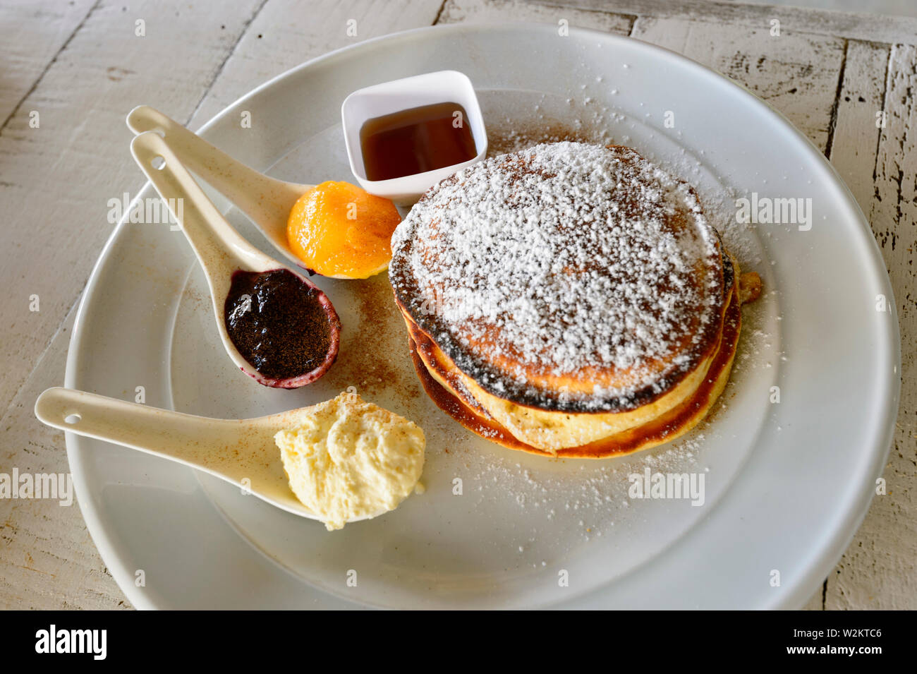 A white plate with pancakes, jam, maple syrup and icing sugar, Rarotonga, Cook Islands, Polynesia Stock Photo