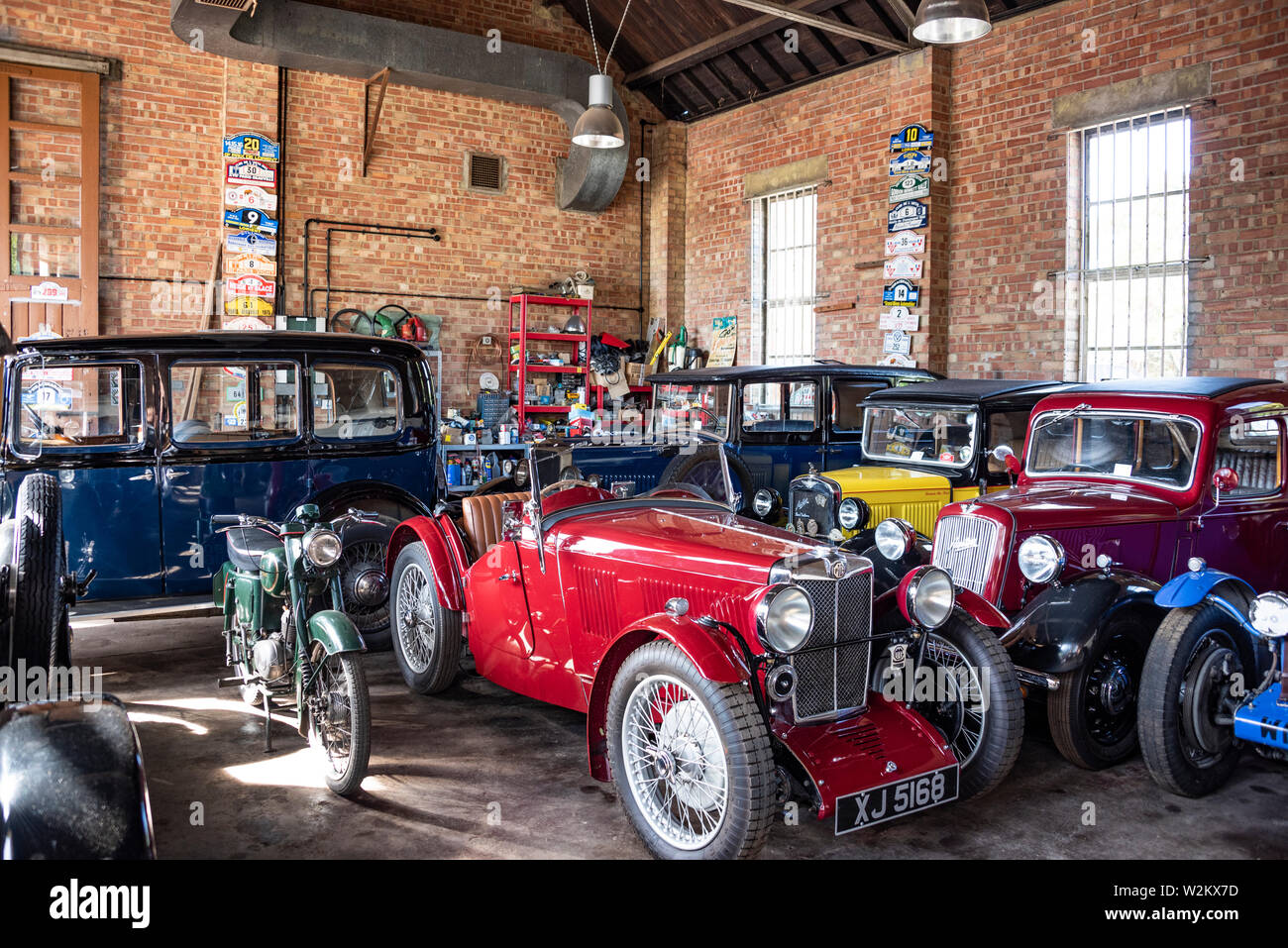 Vintage cars including a rare 1923 MG J2 Midget and Austins parked in a garage at Bicester Heritage, UK Stock Photo