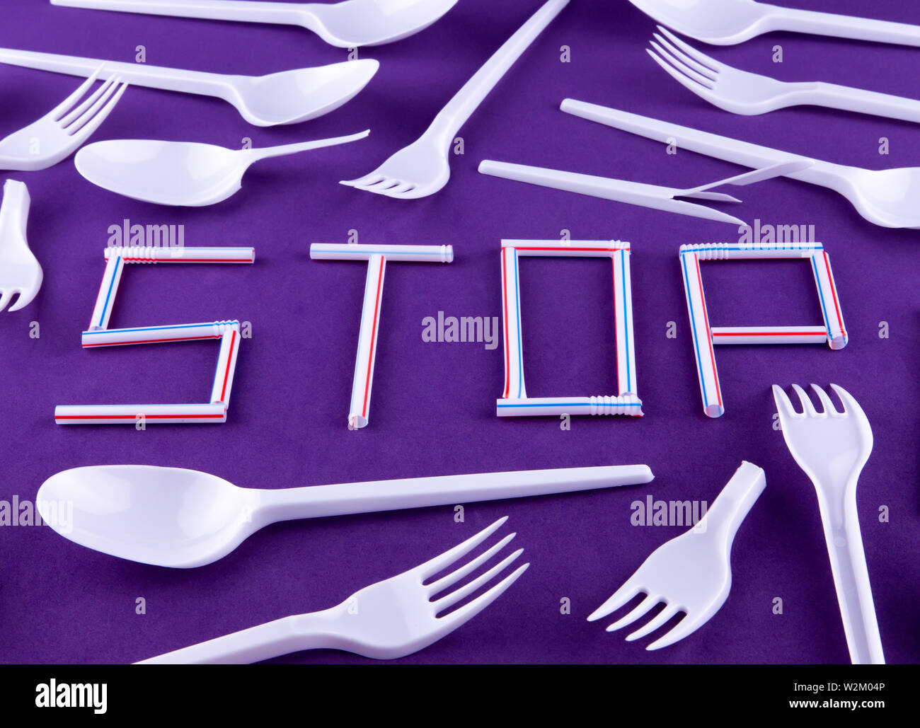 The word stop made of plastic tubes on a purple background with plastic utensils environmental