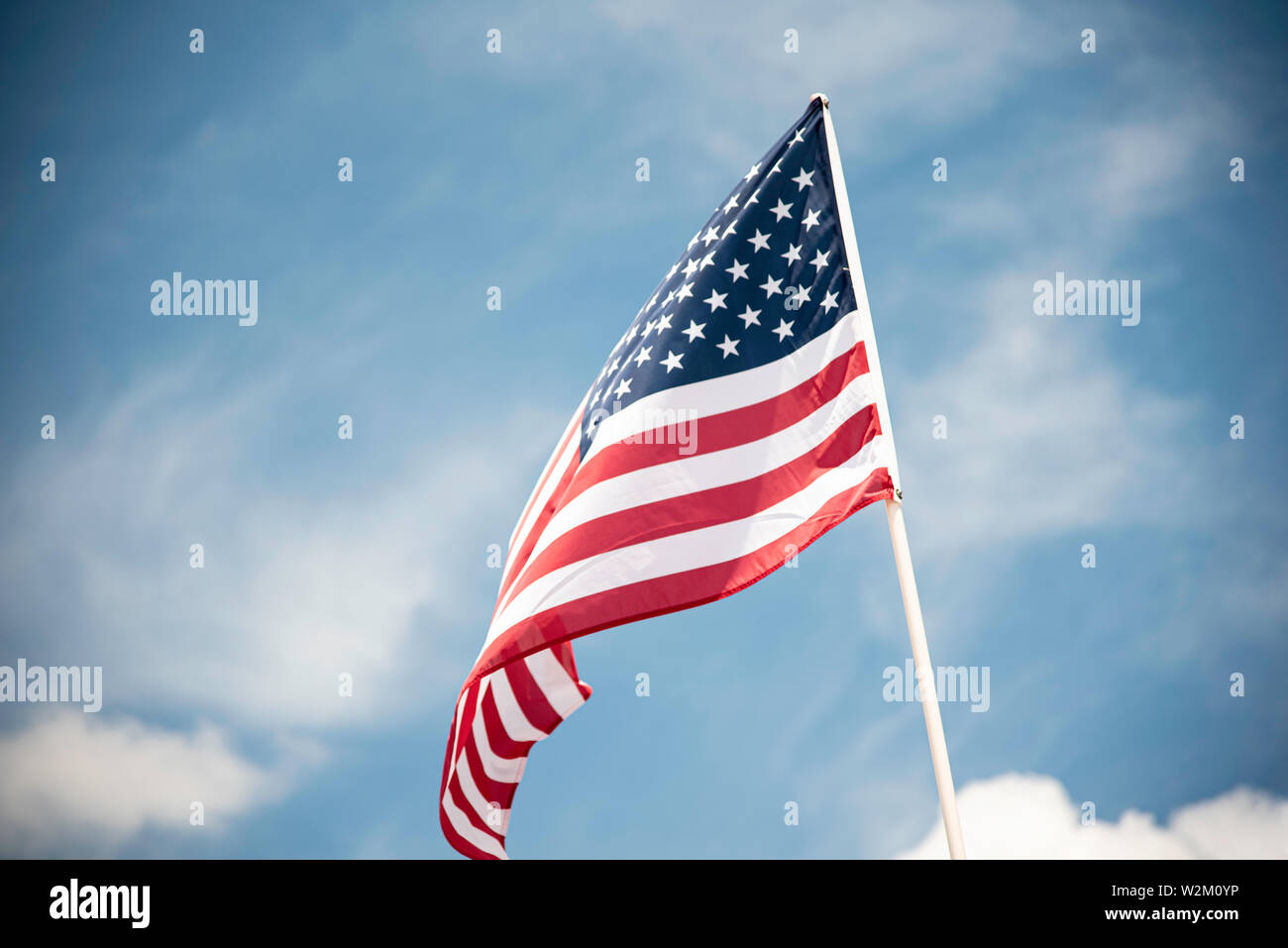 An American flag fluttering in the wind against a blue sky with clouds ...