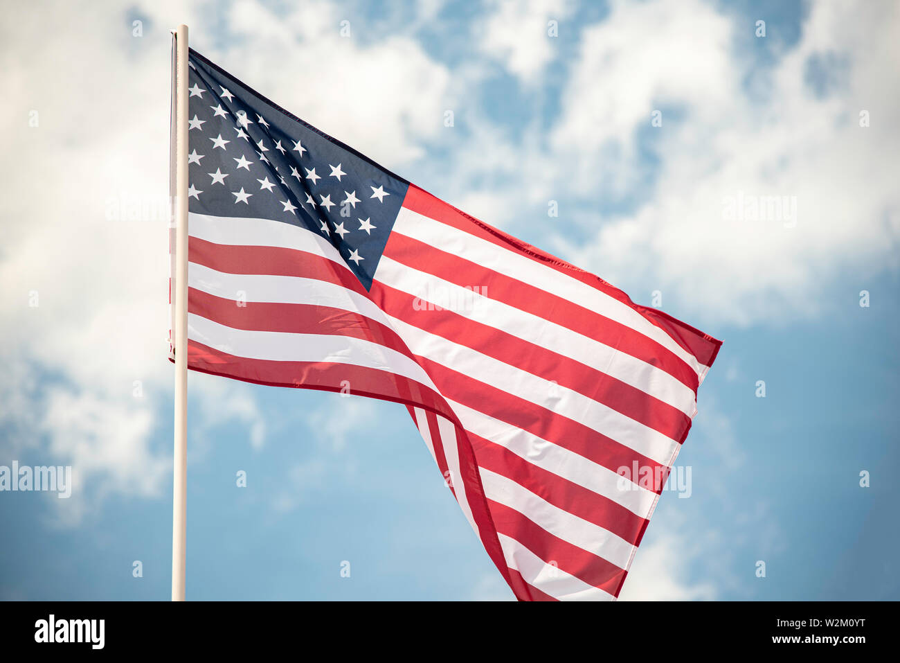 An American flag fluttering in the wind against a blue sky with clouds ...