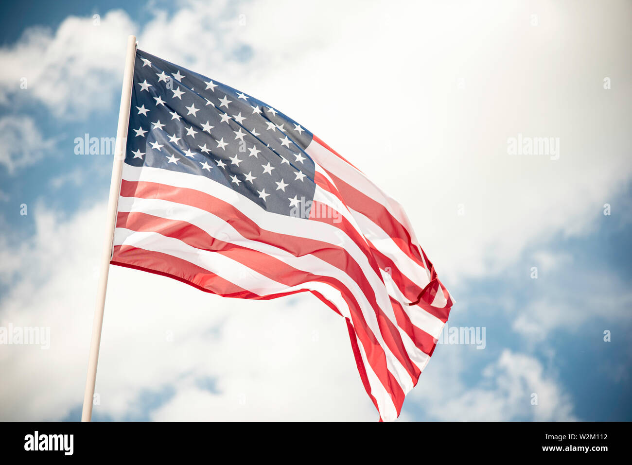 An American flag fluttering in the wind against a blue sky with clouds ...