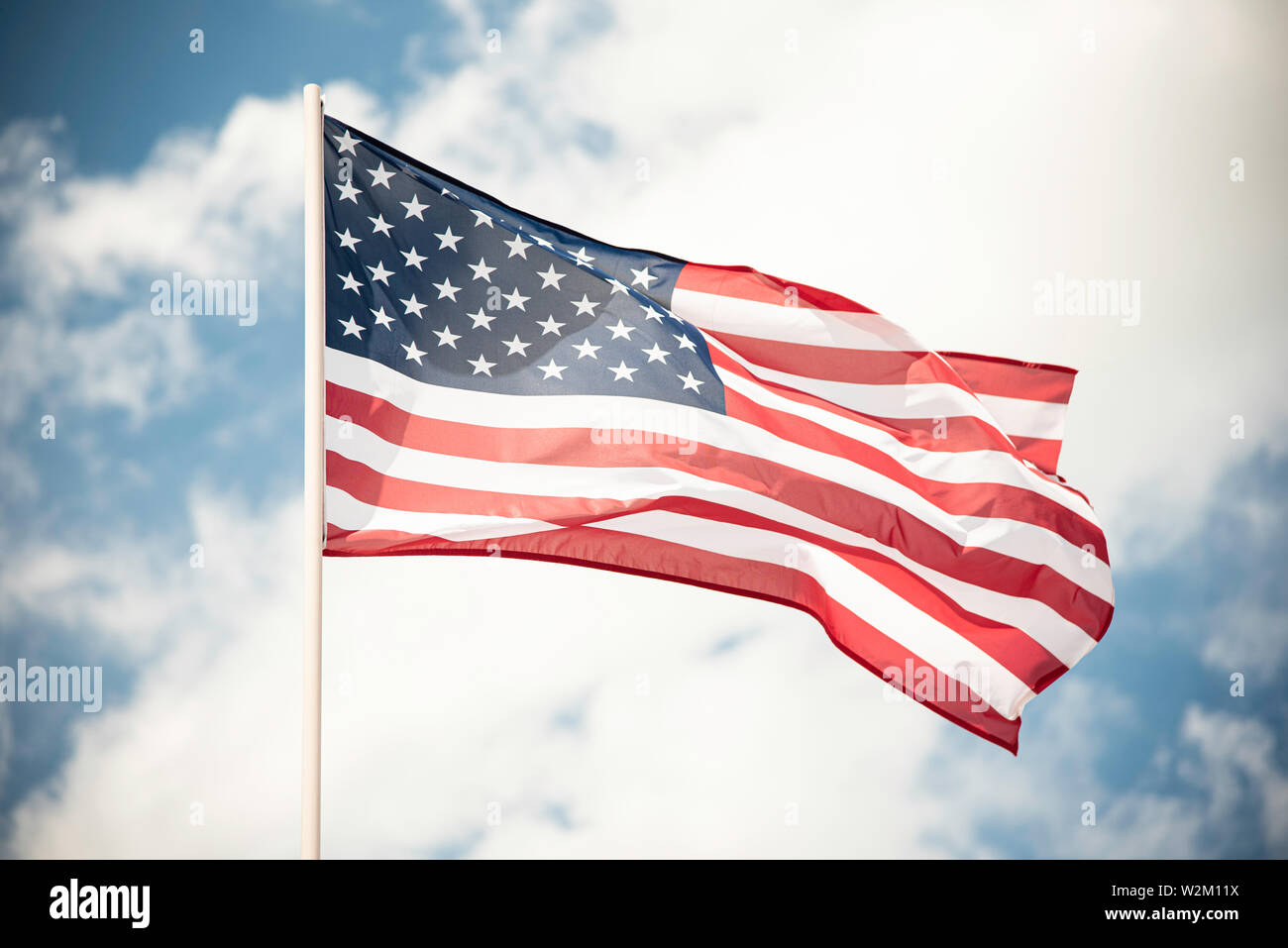An American flag fluttering in the wind against a blue sky with clouds ...