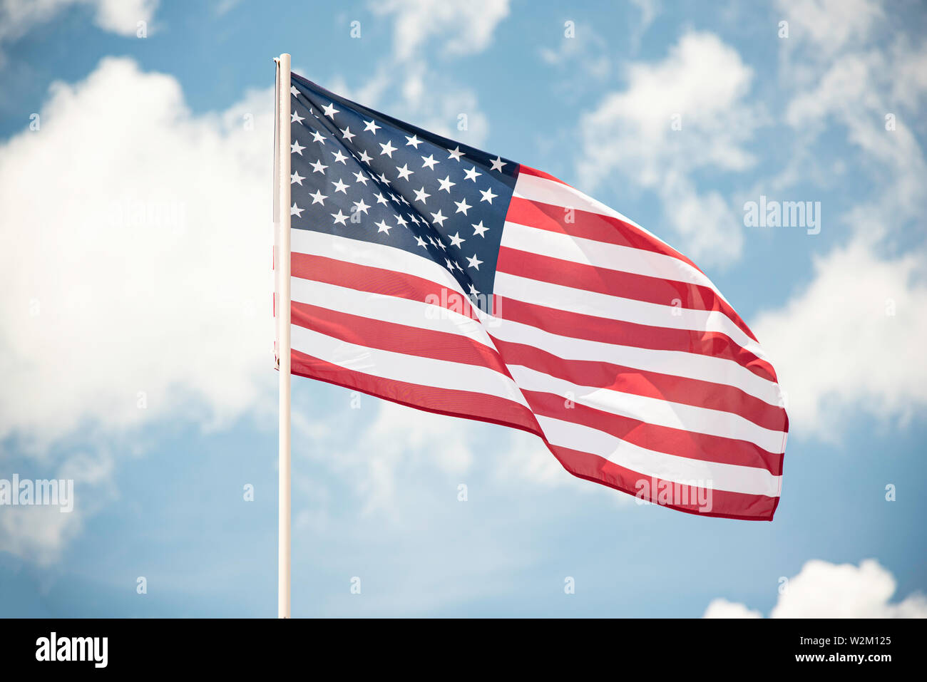 An American flag fluttering in the wind against a blue sky with clouds ...