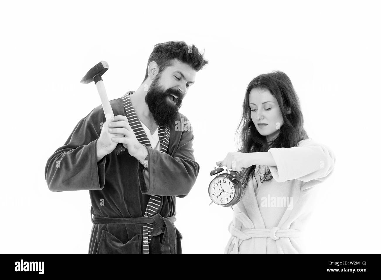 Lets get rid of this annoying alarm clock. Couple in bathrobes going to destroy alarm clock and stay at home. Breaking rules. Tired of early awakening. Man with hammer beat alarm clock. Hateful sound. Stock Photo