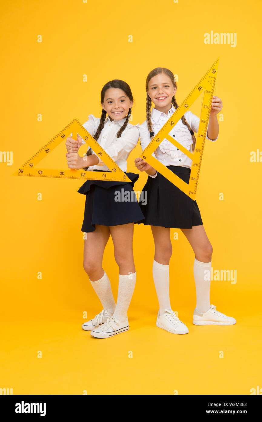 geometric shapes. pupils use gon ruler. stem disciplines. back to school. Maths and geometry. Kids in uniform at yellow wall. friendship and sisterhood. happy small girls study mathematics. Stock Photo