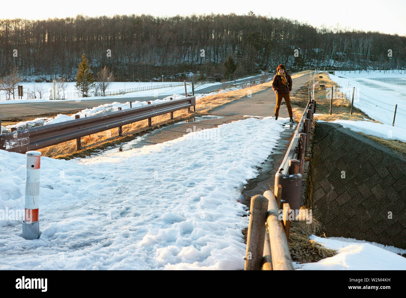 An older lady taking care to walk across a snowy and icy bridge. Stock Photo