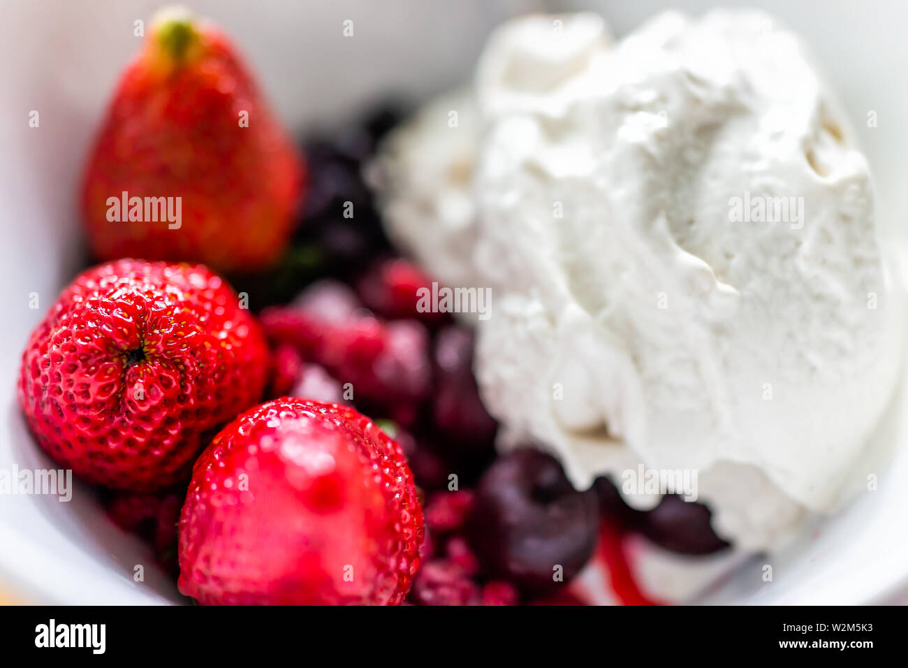 Macro closeup of colorful bowl of vanilla ice cream topped with fresh red strawberry large berries Stock Photo