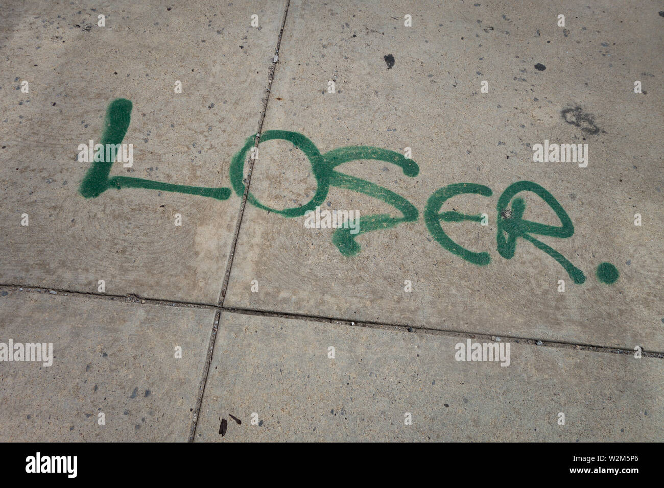 The word 'loser' spray painted on a sidewalk in green paint Stock Photo