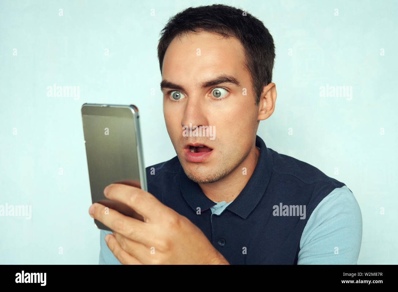 young man looks at the phone and is surprised by what he saw. Puzzled frightened expression on the face of a guy reading the news on the phone Stock Photo