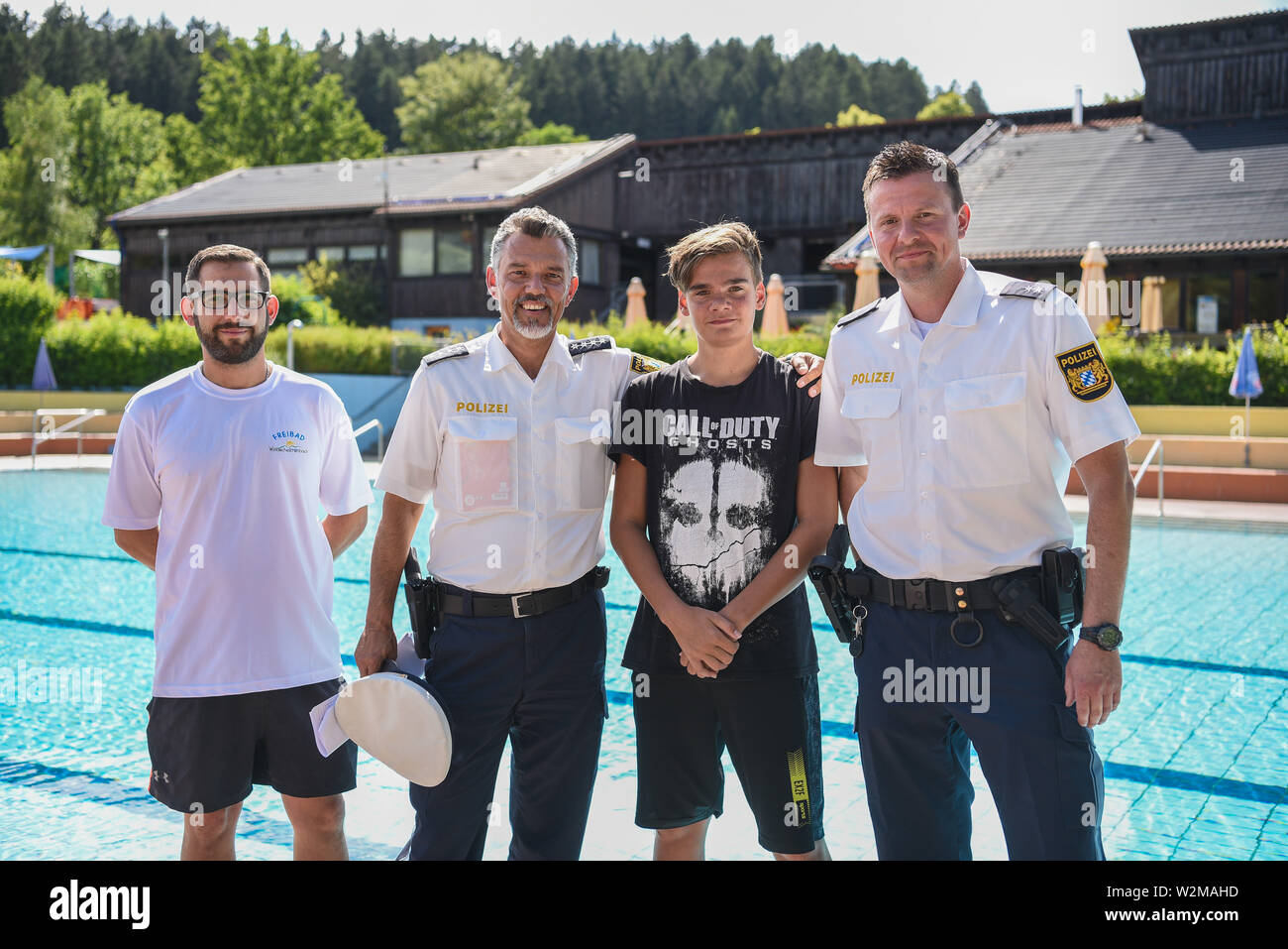 Windischeschenbach, Germany. 08th July, 2019. The 13-year-old Justin Fischer (2nd from right) stands together with bath attendant Benjamin Höllerer (l) and the two policemen Michael Mutzbauer (2nd from left) and Alexander Horn (r) in front of the non-swimmer pool in the outdoor pool. Justin saved a four-year-old boy's life on June 4. He noticed the boy at the bottom of the non-swimmer's pool, pulled him out of the water and called adults for help, who immediately started a cardiac massage. Credit: Nicolas Armer/dpa/Alamy Live News Stock Photo