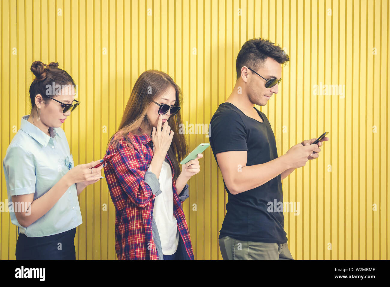 Group of young friends using smart phone against yellow wall ,people addicted by mobile smartphone concept Stock Photo
