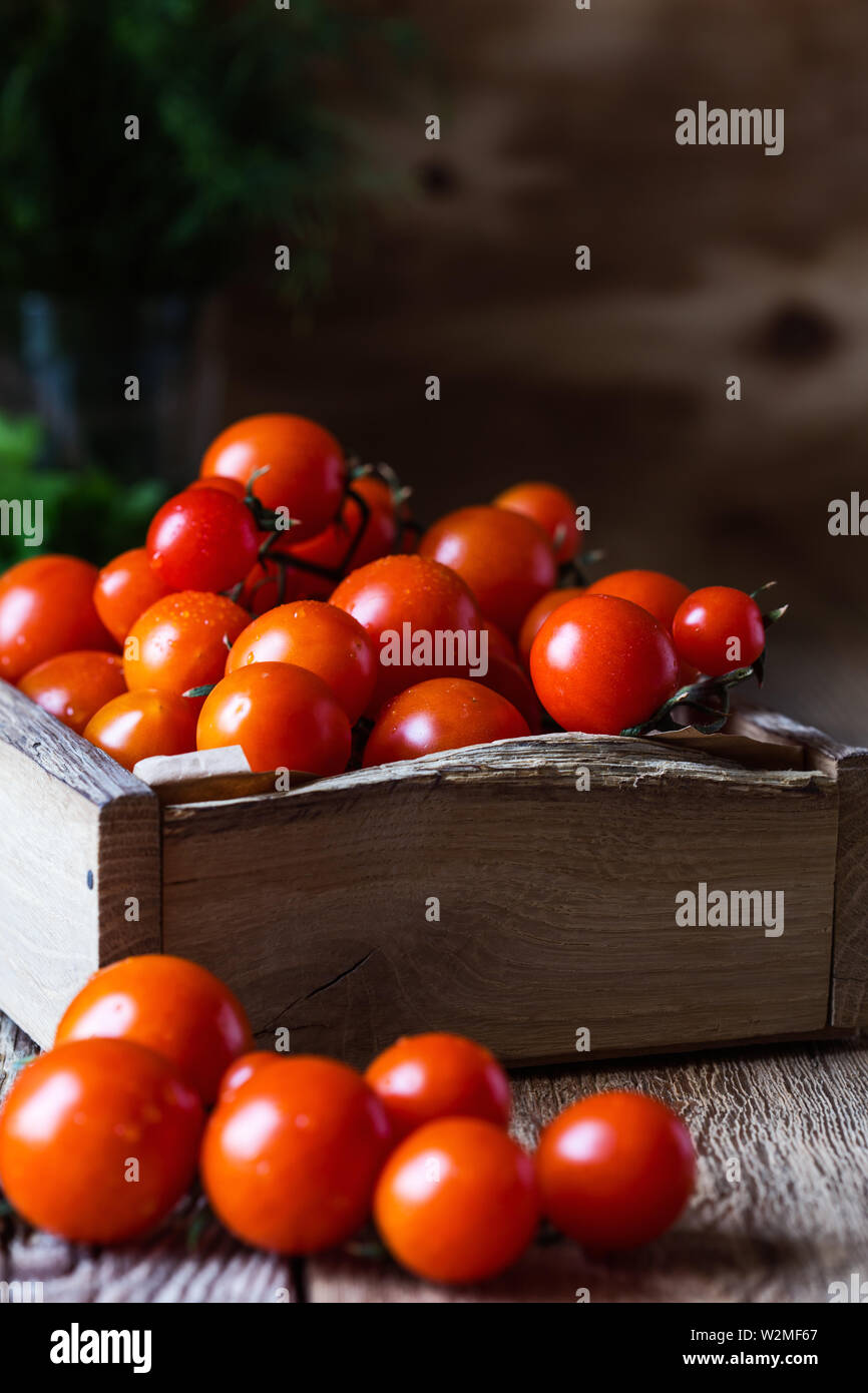Crate of freshly picked organic red cherry  tomatoes on rustic wooden table, plant based food, close up, selective focus Stock Photo