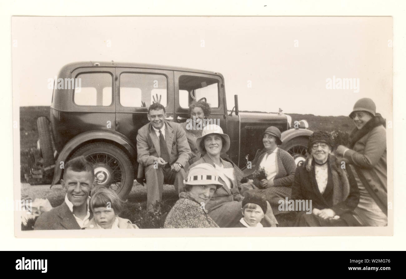 1920s photo of family or friends dressed in smart clothes, suits, cloche hats, having fun and messing about on an excursion next to a vintage car, U.K. Stock Photo