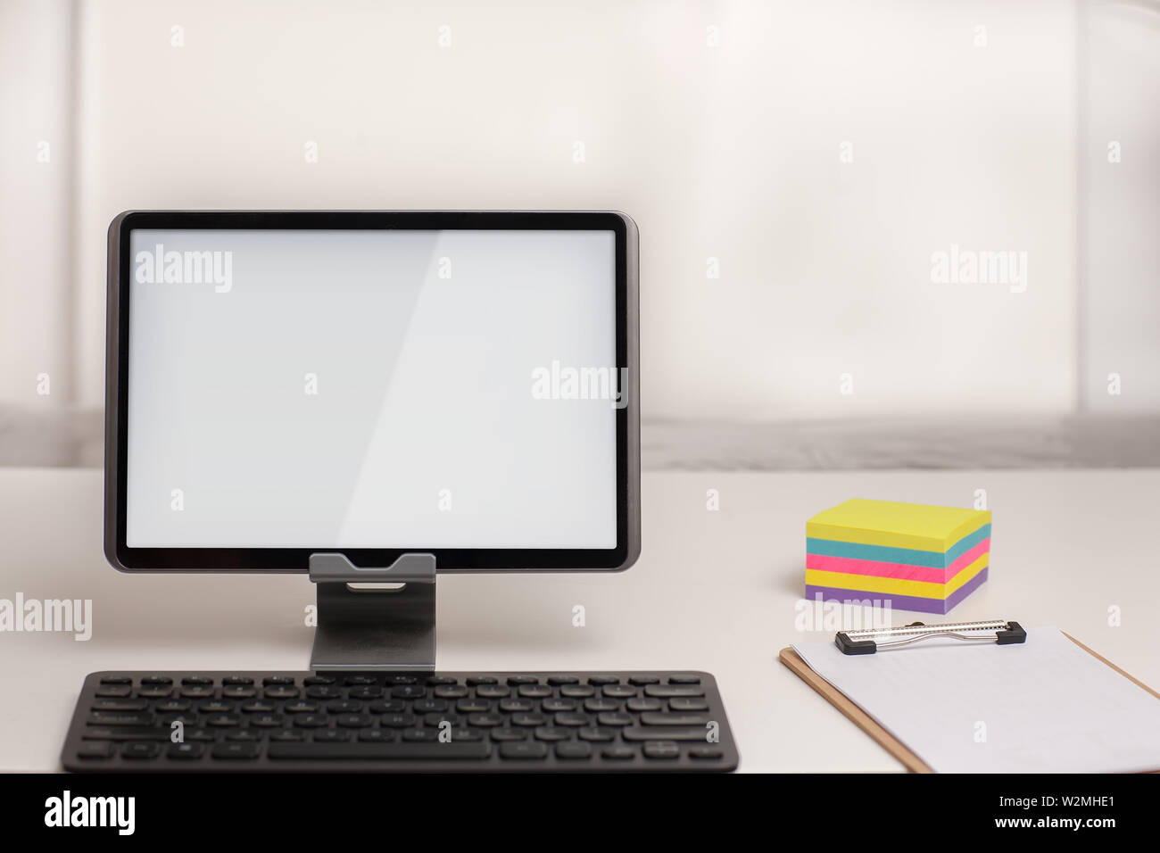 A tablet with a wireless keyboard, on a white desk with note taking office supplies. Stock Photo