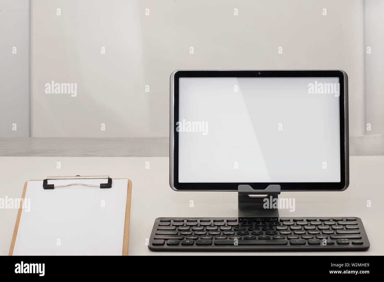 A 10 inch tablet with wireless keyboard and clipboard with paper in a empty office room. Stock Photo