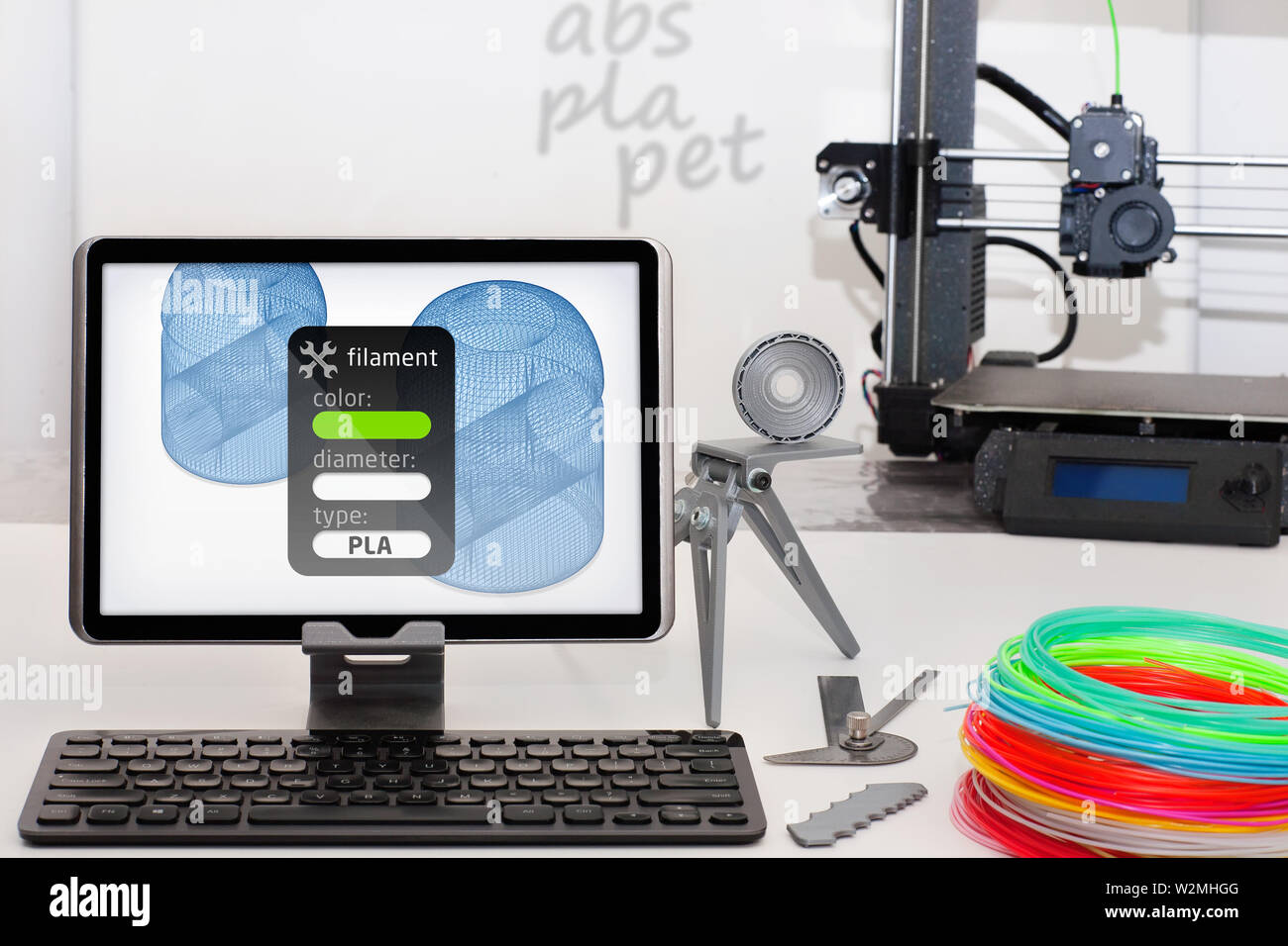 A tablet being used to display 3d printer filament settings and various 3d printer supplies including colorful PLA plastic. Stock Photo