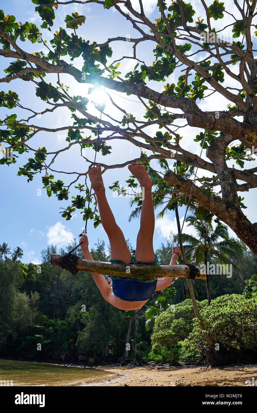 A boy swings on a rope swing from a tree at a tropical beach in scenic