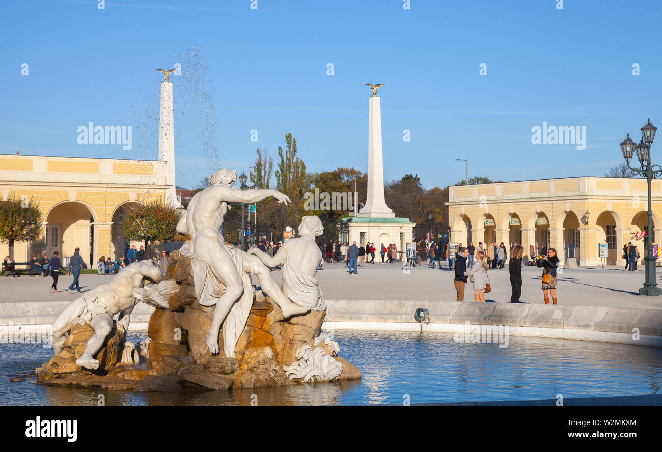 Vienna, Austria - November 1, 2015: People walk near fountain with sculpture at the entrance of the Schonbrunn Palace. It is a former imperial summer Stock Photo