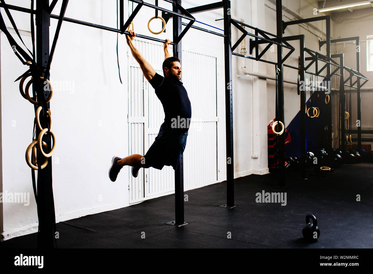Young man doing kipping pull-ups exercise at gym Stock Photo