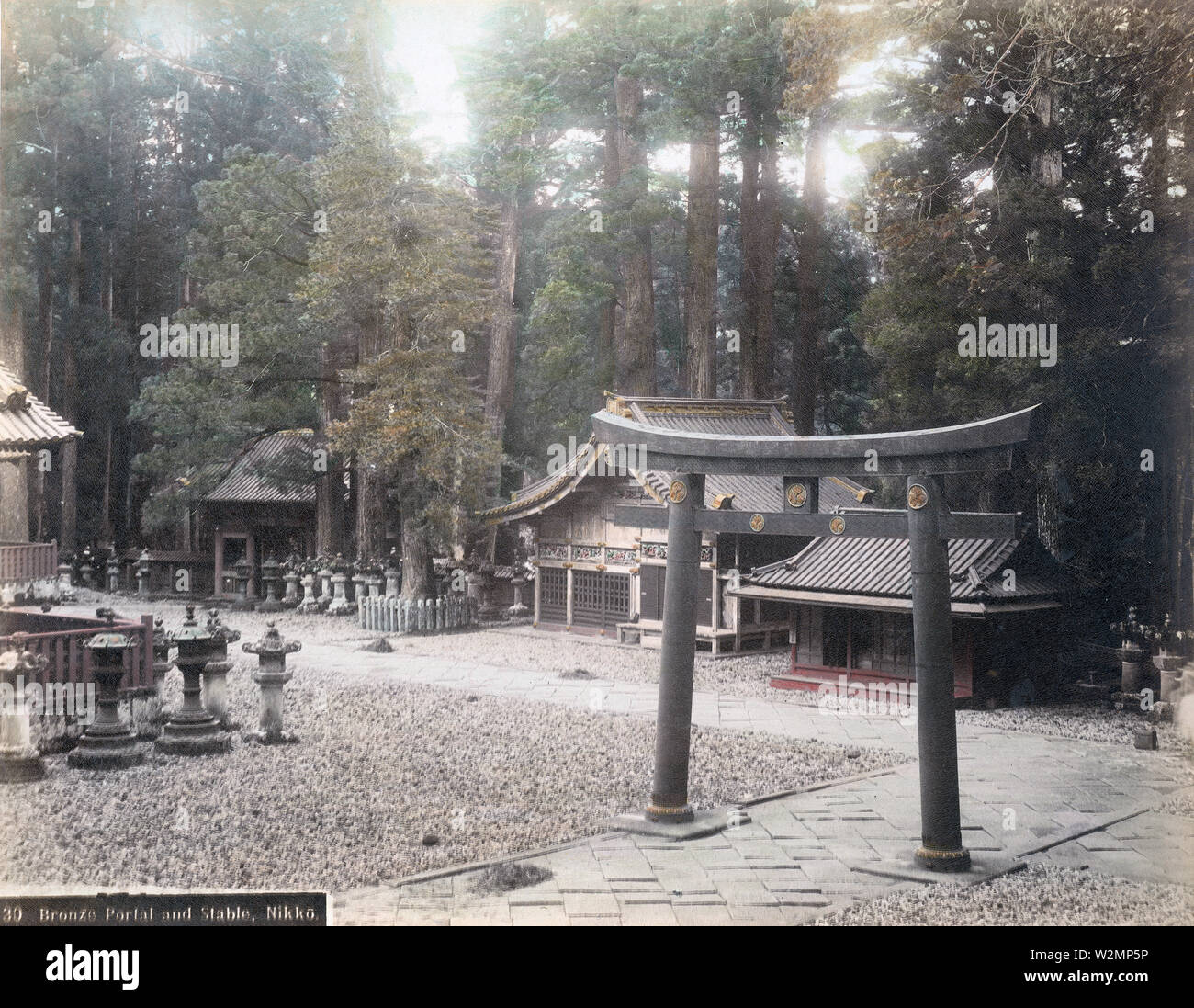 [ 1890s Japan - Sacred Bronze Torii Gate at Nikko ] —   The 6 meter high Karado Torii, the first bronze torii in Japan, as seen from the Yomeimon in Nikko.   The building in the center is Shinkyu, the stable for sacred horses and the only building of plain wood in Toshogu Shrine. The stable features 8 panels with carvings of monkeys, signifying the life of people. Monkeys were believed to be guardians of horses.  19th century vintage albumen photograph. Stock Photo