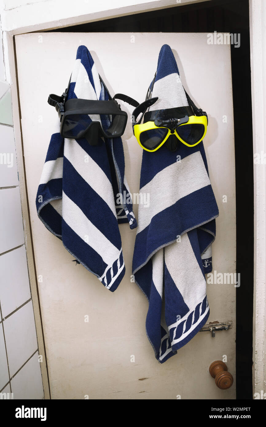 Two striped terry towels with diving masks hang on wooden door in old changing room Stock Photo