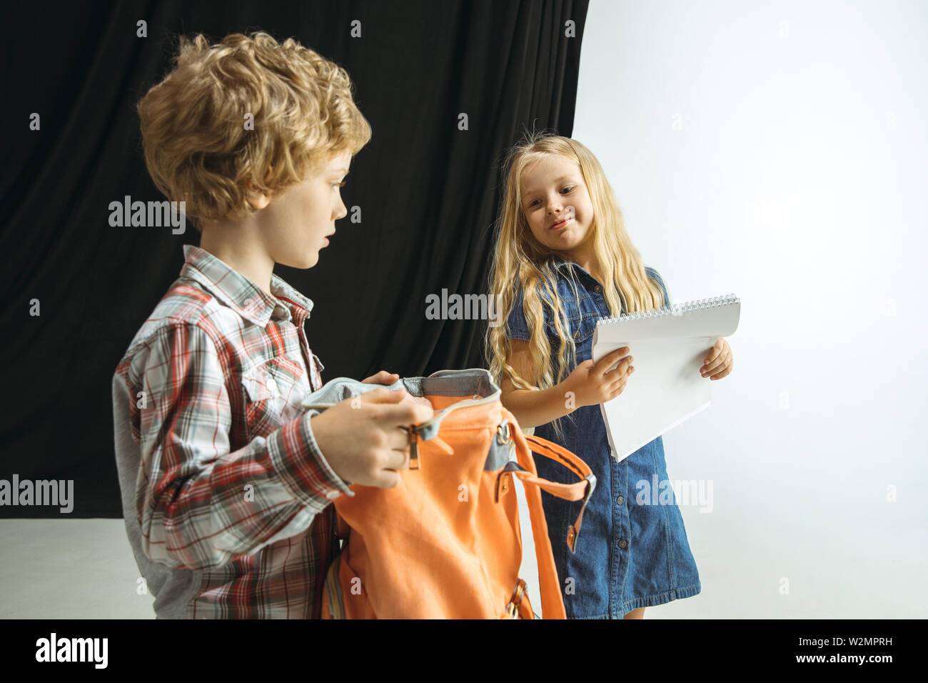 Boy and girl preparing for school after a long summer break. Back to school. Little caucasian models packing a bag together on studio background. Childhood, education, holidays or homework concept. Stock Photo