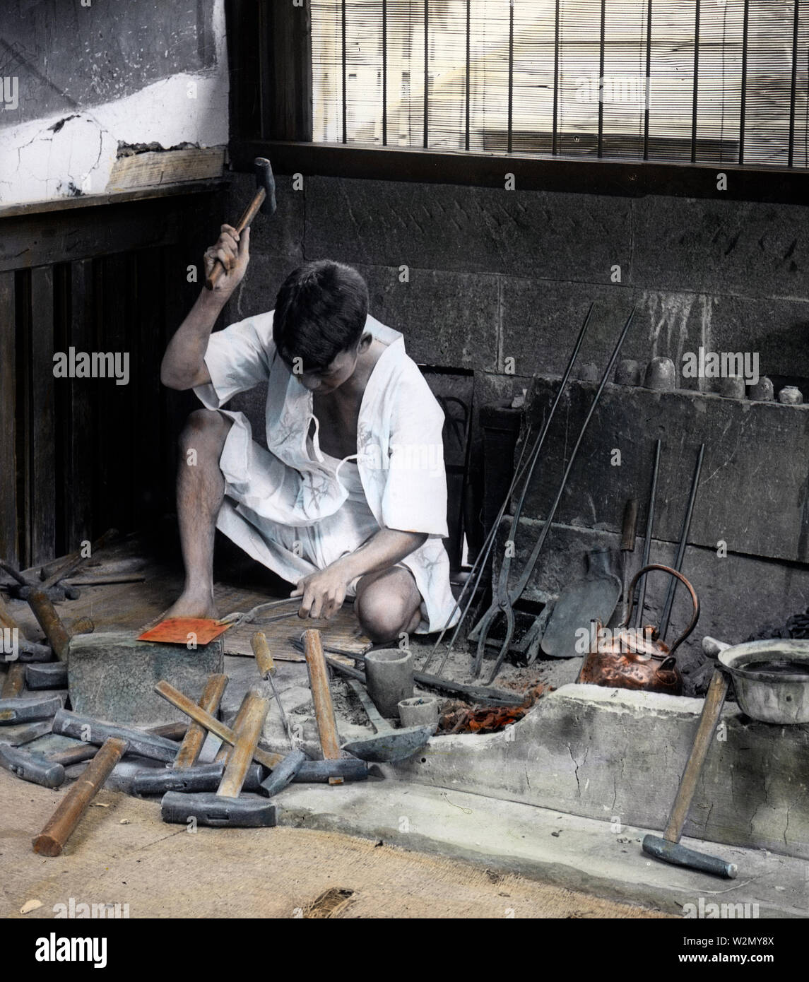 [ 1890s Japan - Japanese Blacksmith at Work ] —   Young Japanese blacksmith sitting down at work.  20th century vintage glass slide. Stock Photo