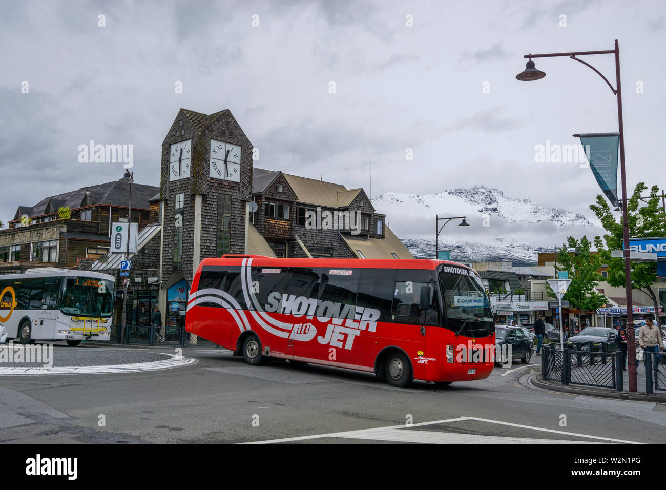 Red tourist coach driving through central Queenstown on cloudy day, Queenstown New Zealand Stock Photo