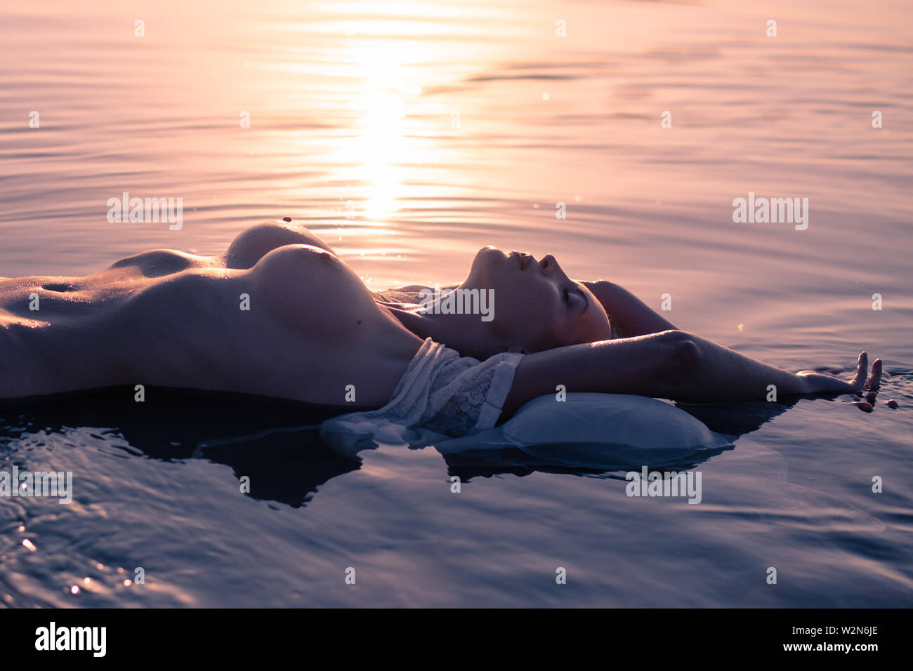Silhouette of a young sexy nude woman with big beautiful breasts lies in  the waves of the reservoir in the rays of the setting sun Stock Photo -  Alamy