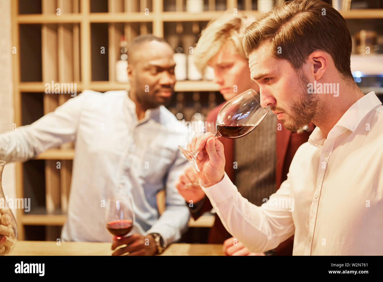 Young man with friends at a wine tasting smells at a glass of red wine Stock Photo
