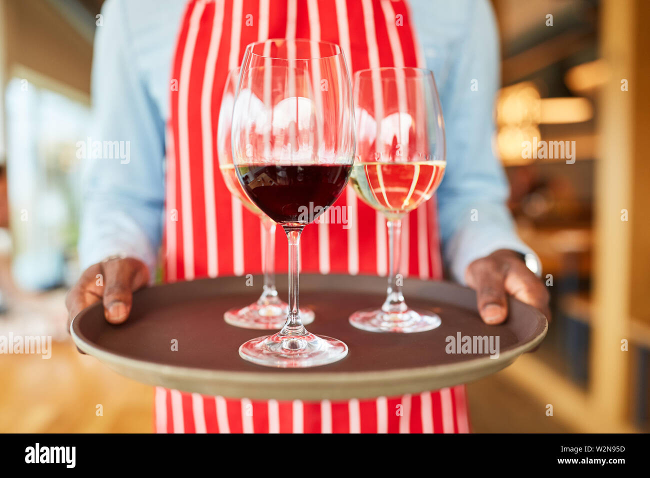 Hands of a waiter carry a tray with glasses of wine in the bistro or