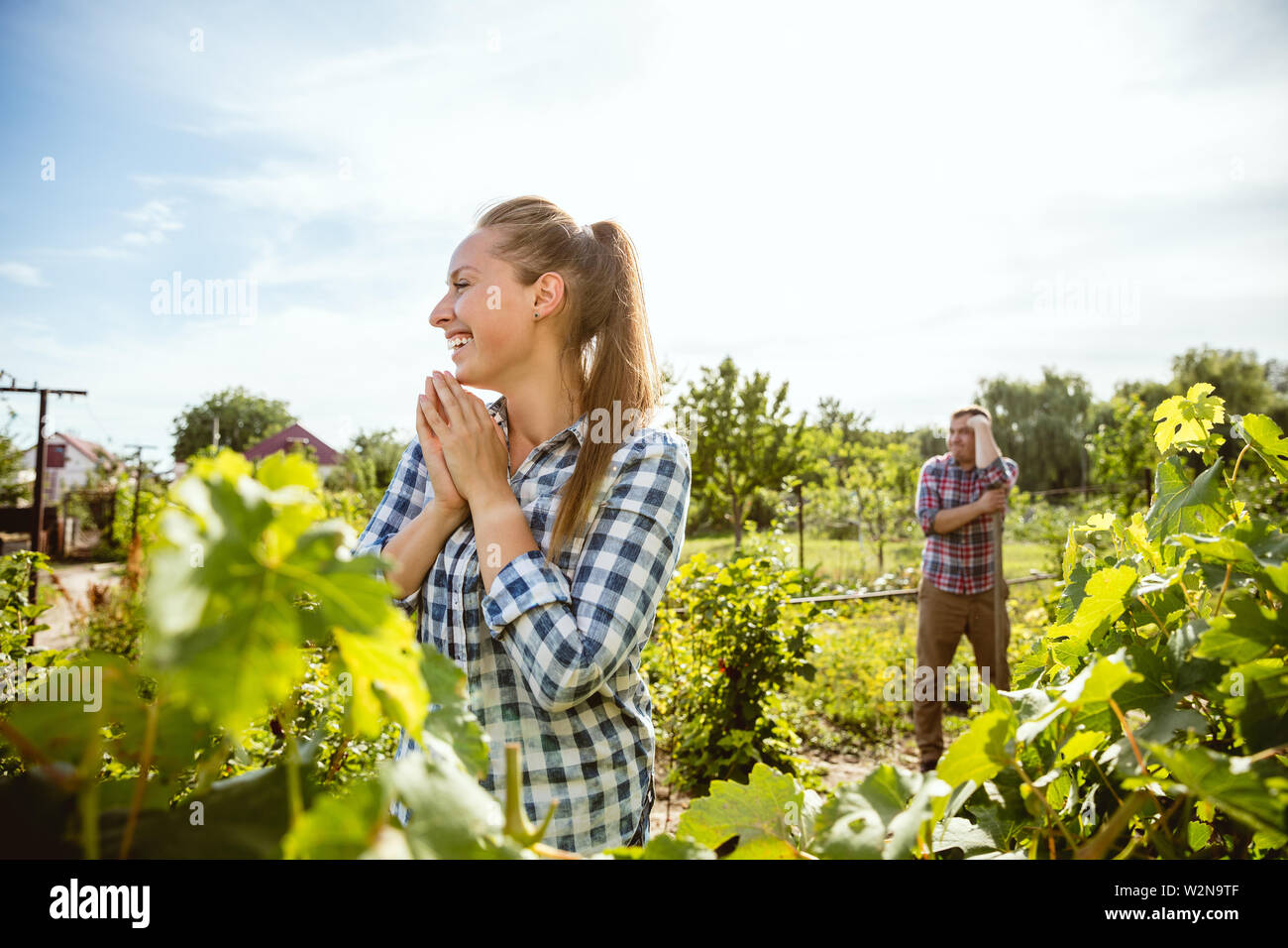 Young and happy farmer's couple at their garden in sunny day. Man and woman engaged in the cultivation of eco friendly products. Concept of farming, agriculture, healthy lifestyle, family occupation. Stock Photo