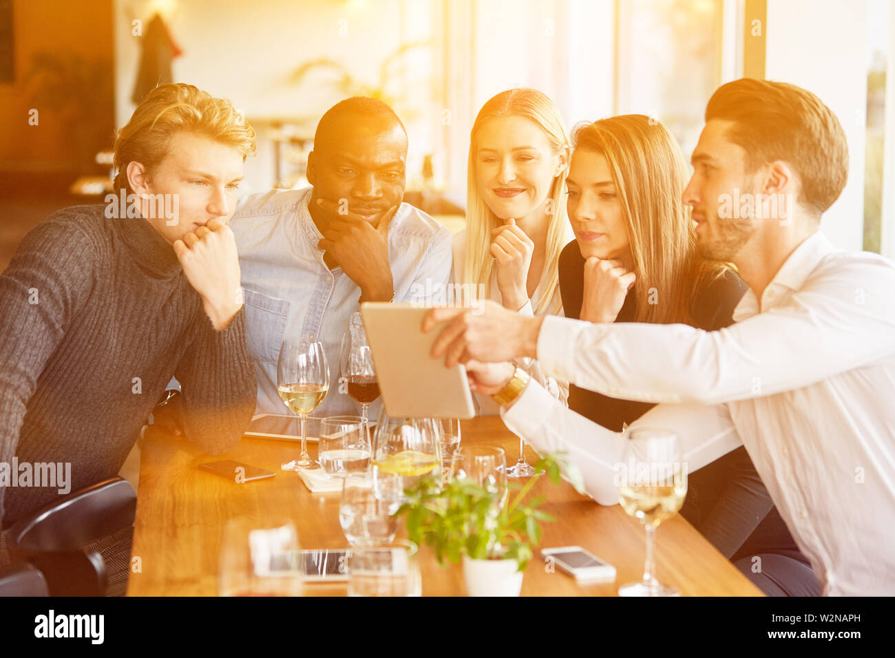 Group at meeting in restaurant looks together on tablet computer Stock Photo