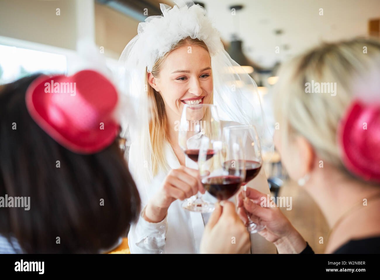 Happy bride with bridal veil while toasting with glass of wine at a