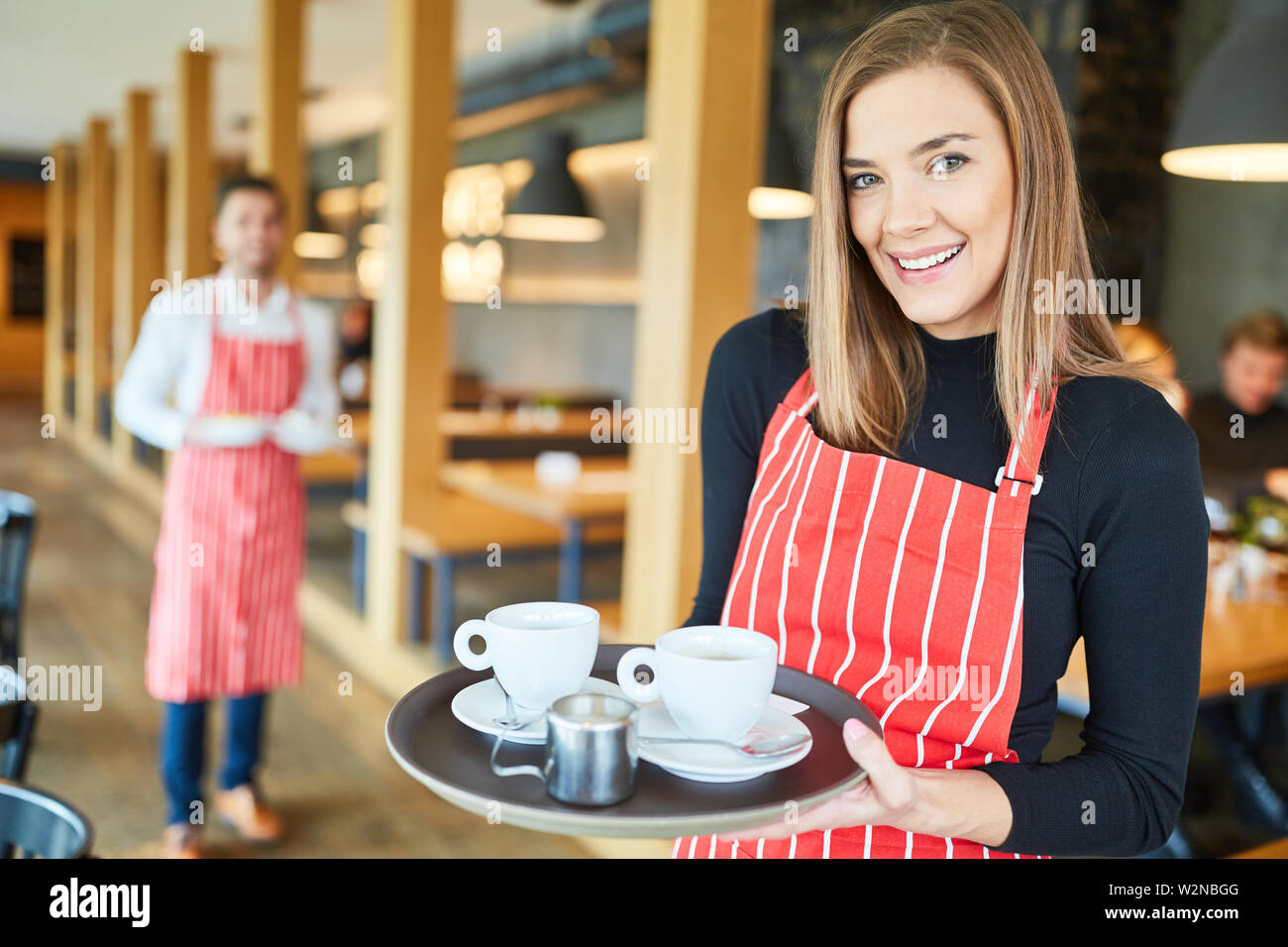 Young woman serving as a waitress in cafe or restaurant carries a tray of coffee cups Stock