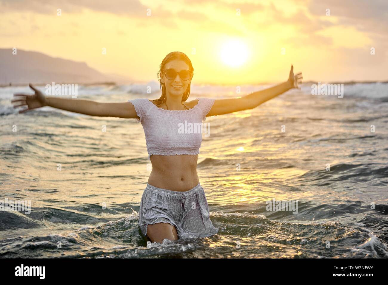 young lively teenage woman with open arms in sea water at beach, wet